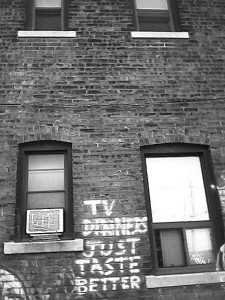 A photograph of a brick wall with graffiti that says But TV Dinners Just Taste Better